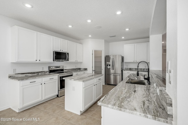 kitchen with a kitchen island, a sink, white cabinetry, appliances with stainless steel finishes, and light stone countertops