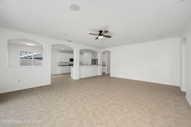 unfurnished living room with baseboards, arched walkways, and a ceiling fan