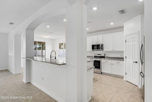 kitchen featuring arched walkways, white cabinets, visible vents, light stone counters, and stainless steel appliances