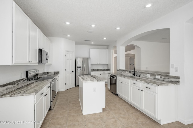 kitchen featuring light stone counters, a sink, white cabinets, appliances with stainless steel finishes, and a center island