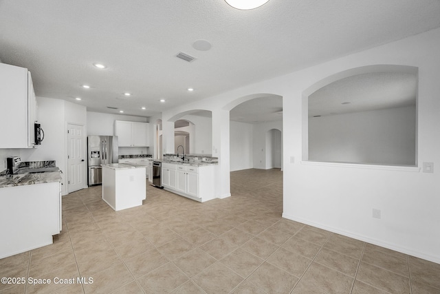 kitchen featuring light stone counters, a center island, stainless steel appliances, white cabinets, and a sink