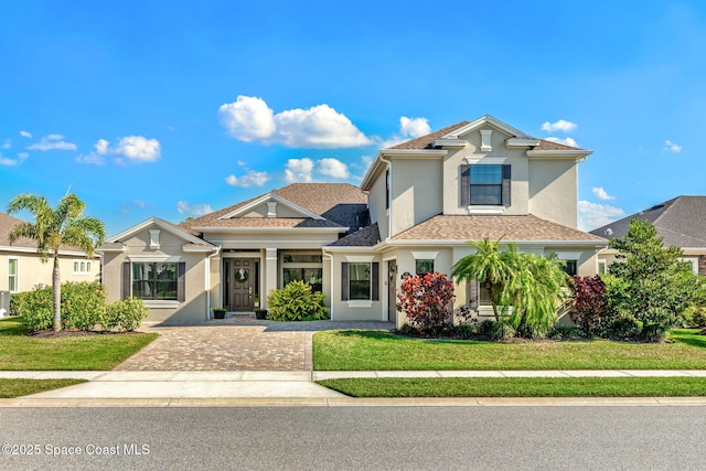 view of front of property with a shingled roof, a front yard, and stucco siding