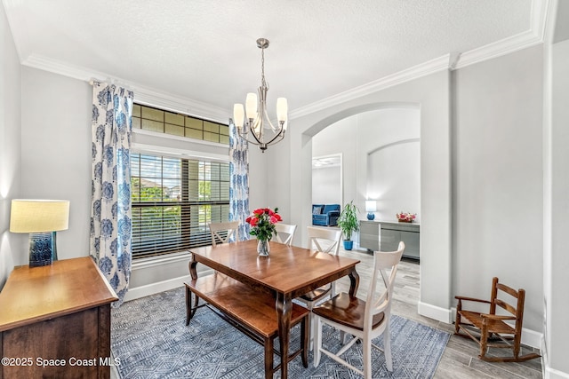 dining area featuring a textured ceiling, ornamental molding, wood finished floors, and a notable chandelier