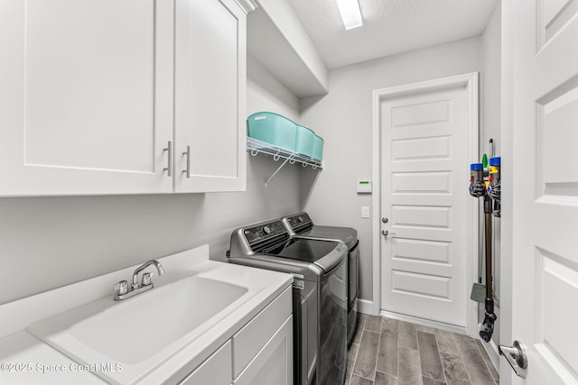 clothes washing area with a textured ceiling, separate washer and dryer, a sink, cabinet space, and wood tiled floor