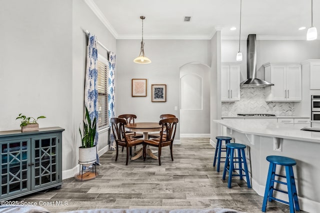 interior space with tasteful backsplash, visible vents, wall chimney exhaust hood, light wood-style flooring, and a kitchen bar