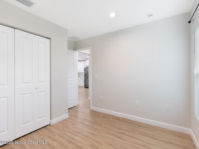 unfurnished bedroom with a closet, light hardwood / wood-style floors, and stainless steel fridge with ice dispenser