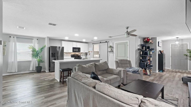 living room with sink, light wood-type flooring, ceiling fan, a barn door, and a textured ceiling