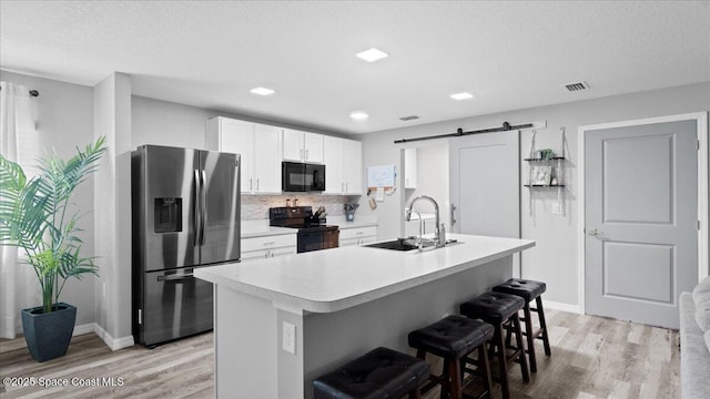 kitchen featuring sink, a breakfast bar area, black appliances, a center island with sink, and a barn door