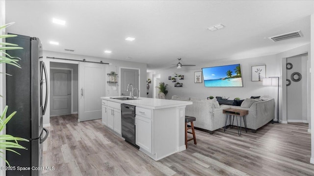 kitchen featuring sink, white cabinetry, stainless steel fridge, a barn door, and a kitchen island with sink