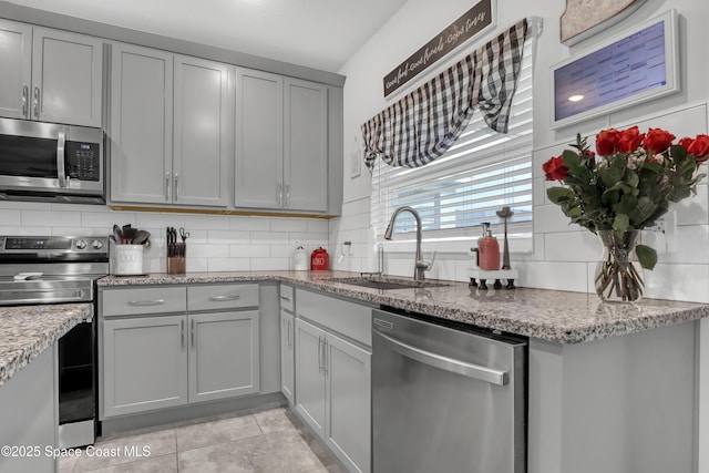 kitchen featuring sink, gray cabinetry, light stone counters, stainless steel appliances, and backsplash