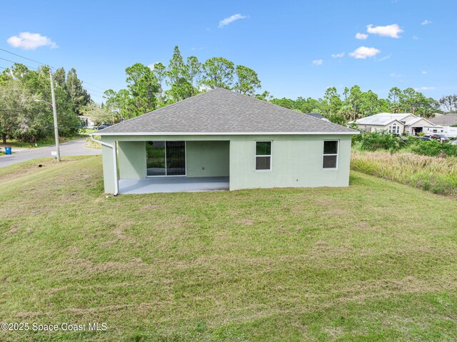 rear view of property featuring stucco siding, roof with shingles, a patio, and a lawn