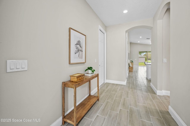 hall featuring arched walkways, light wood finished floors, recessed lighting, and baseboards