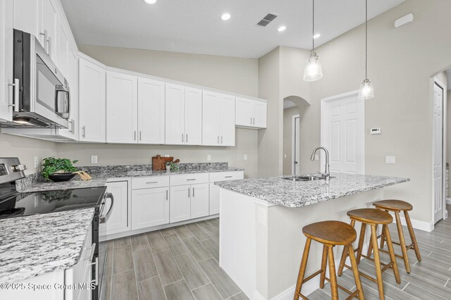 kitchen with arched walkways, visible vents, white cabinetry, appliances with stainless steel finishes, and an island with sink