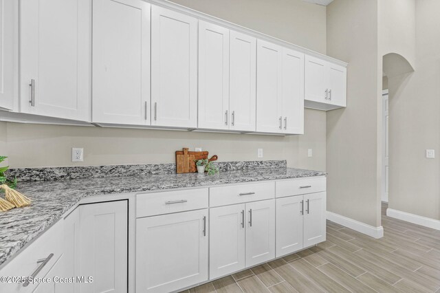 kitchen featuring baseboards, arched walkways, light stone counters, wood tiled floor, and white cabinetry