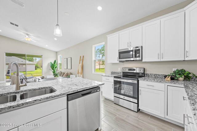 kitchen with light stone counters, a sink, white cabinetry, hanging light fixtures, and appliances with stainless steel finishes