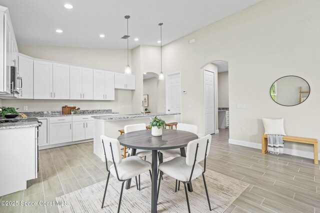 kitchen featuring arched walkways, white cabinetry, hanging light fixtures, light stone countertops, and a center island with sink