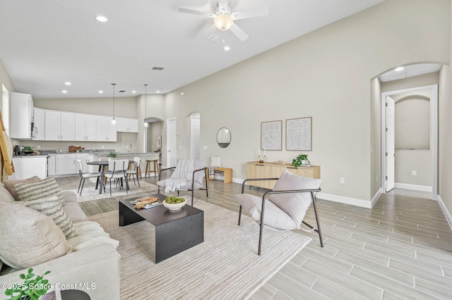 living area with baseboards, arched walkways, ceiling fan, and wood finish floors