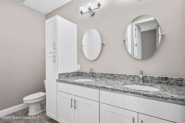 bathroom featuring baseboards, a sink, toilet, and double vanity