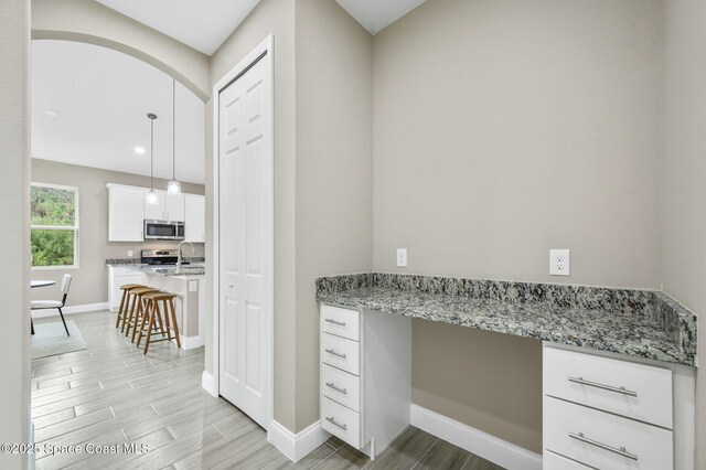 kitchen featuring appliances with stainless steel finishes, built in study area, light stone countertops, and white cabinets