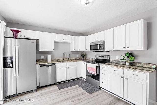 kitchen with sink, light hardwood / wood-style flooring, appliances with stainless steel finishes, light stone countertops, and white cabinets