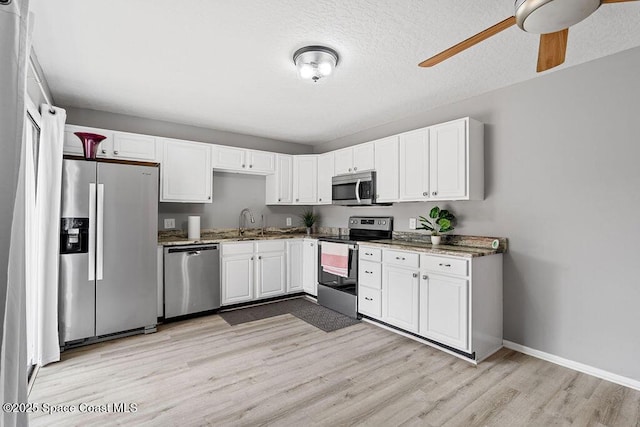 kitchen with white cabinetry, sink, dark stone countertops, stainless steel appliances, and light wood-type flooring