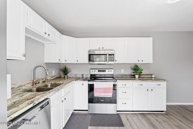 kitchen featuring appliances with stainless steel finishes, white cabinetry, sink, light stone counters, and light hardwood / wood-style flooring