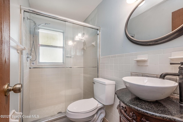 full bathroom featuring a stall shower, wainscoting, toilet, vanity, and tile walls