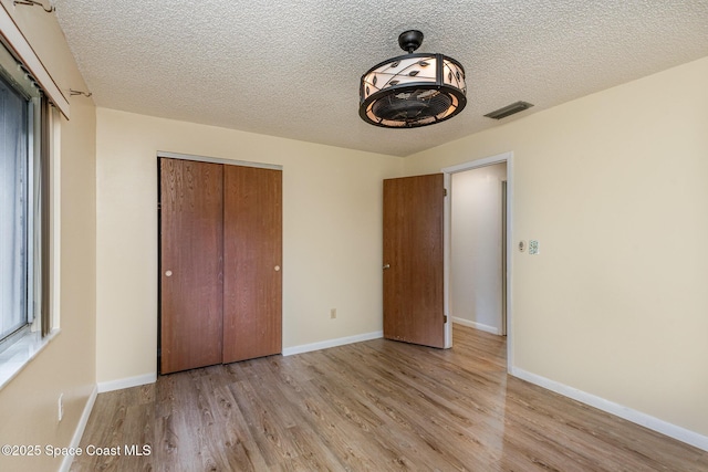 unfurnished bedroom with light wood-style floors, baseboards, visible vents, and a closet