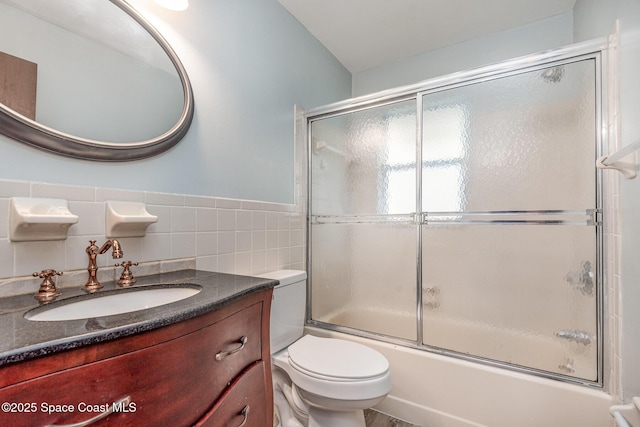 full bathroom featuring toilet, a wainscoted wall, enclosed tub / shower combo, vanity, and tile walls