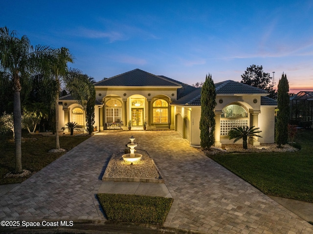 mediterranean / spanish house with a tile roof, french doors, decorative driveway, and stucco siding