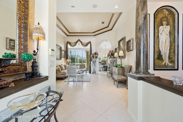 interior space featuring ornamental molding, arched walkways, a tray ceiling, and light tile patterned floors