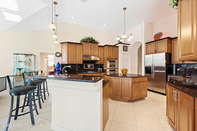 kitchen with light tile patterned floors, arched walkways, a kitchen island, appliances with stainless steel finishes, and under cabinet range hood