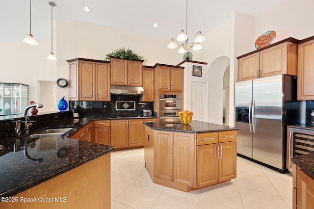 kitchen with arched walkways, high vaulted ceiling, under cabinet range hood, a sink, and appliances with stainless steel finishes