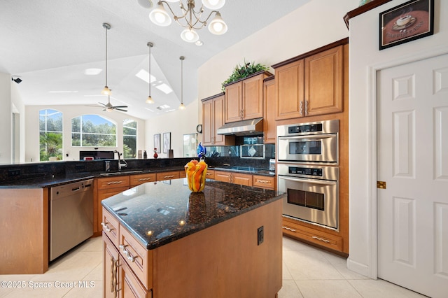 kitchen with under cabinet range hood, stainless steel appliances, a peninsula, a sink, and lofted ceiling with skylight