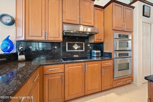 kitchen featuring tasteful backsplash, dark stone counters, black electric stovetop, under cabinet range hood, and light tile patterned flooring