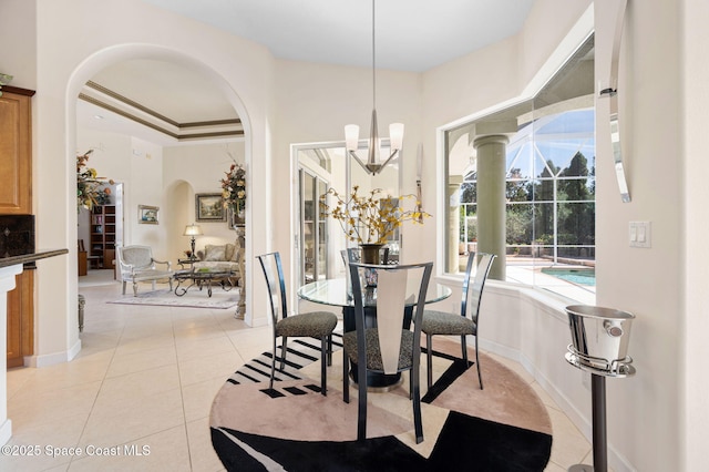 dining room featuring light tile patterned floors, baseboards, arched walkways, a raised ceiling, and an inviting chandelier