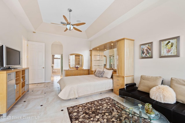 bedroom with a towering ceiling, arched walkways, a raised ceiling, and connected bathroom