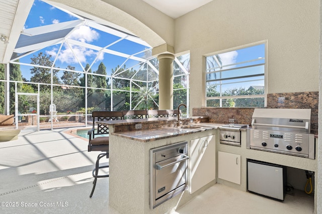 view of patio with outdoor dry bar, grilling area, a sink, exterior kitchen, and a lanai