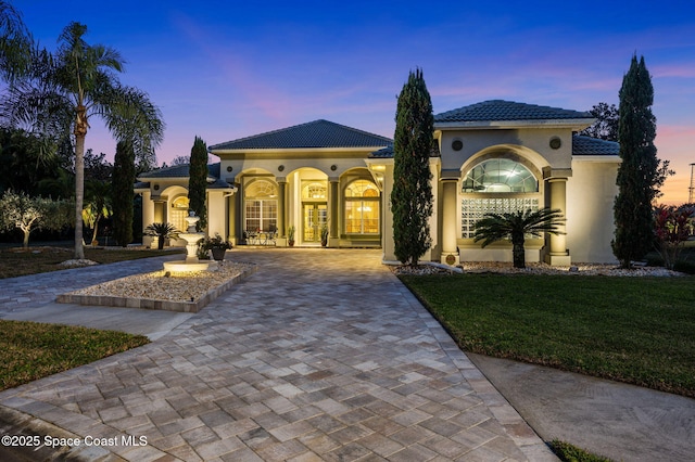 mediterranean / spanish-style home featuring a tile roof, french doors, decorative driveway, and stucco siding