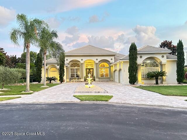 mediterranean / spanish-style house featuring decorative driveway, stucco siding, a garage, a tiled roof, and a front lawn