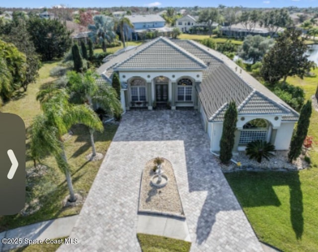 view of front of house with a front lawn, decorative driveway, a tile roof, and stucco siding