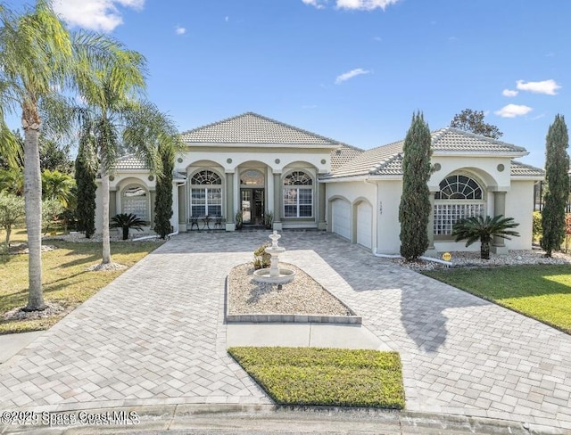 mediterranean / spanish-style house featuring a garage, a tile roof, decorative driveway, and stucco siding