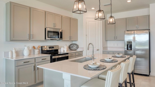 kitchen with gray cabinets, sink, hanging light fixtures, stainless steel appliances, and a center island with sink