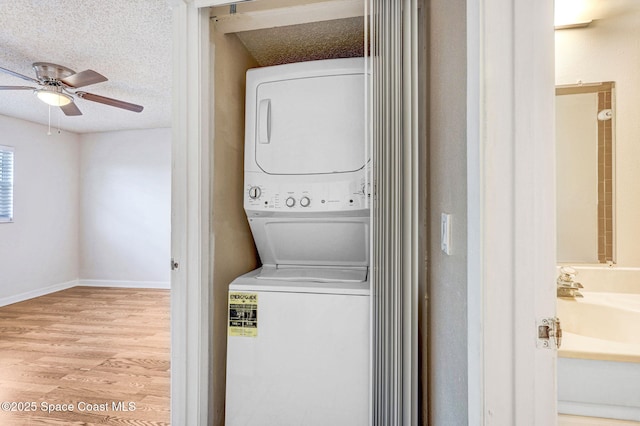 laundry area with ceiling fan, stacked washing maching and dryer, a textured ceiling, and light hardwood / wood-style flooring