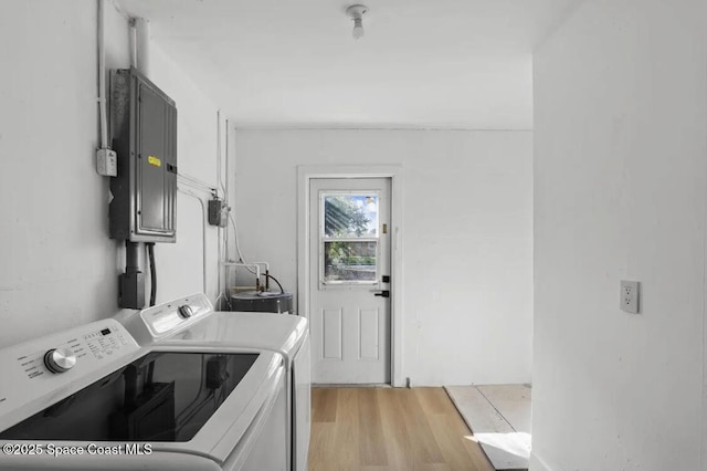 laundry area with electric panel, washer and dryer, and light wood-type flooring