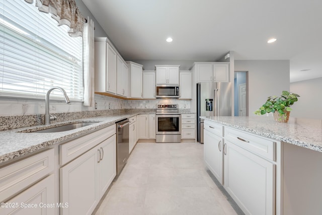 kitchen with light stone counters, sink, white cabinets, and appliances with stainless steel finishes