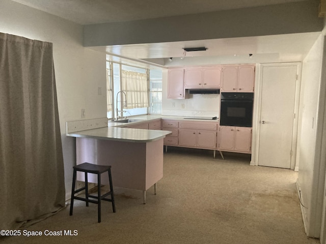 kitchen with a peninsula, a sink, black appliances, under cabinet range hood, and a kitchen bar