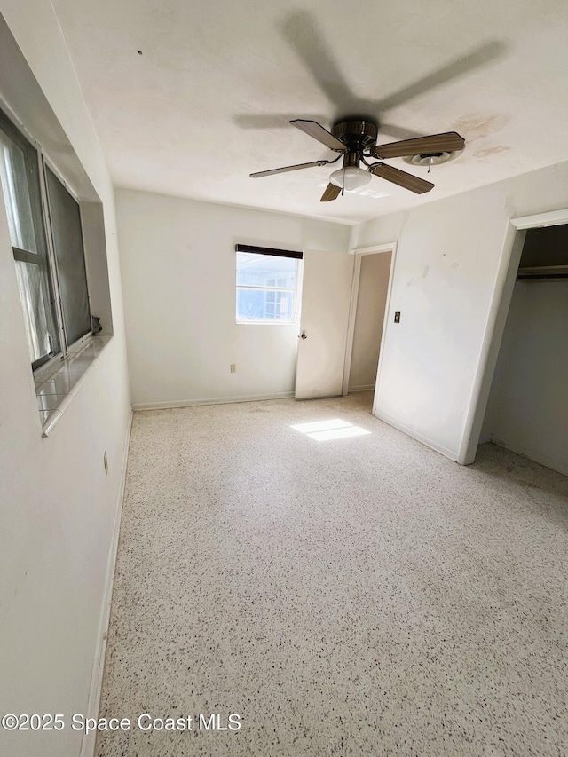 unfurnished bedroom featuring baseboards, speckled floor, and ceiling fan