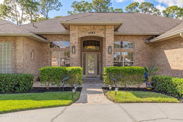 property entrance with brick siding, a lawn, and a shingled roof