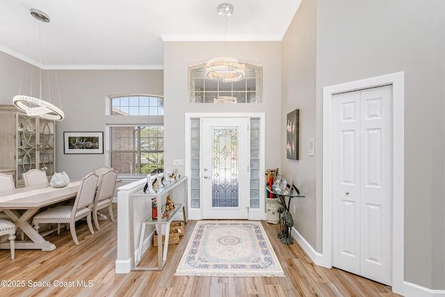 foyer featuring a towering ceiling, crown molding, light wood-style flooring, and baseboards